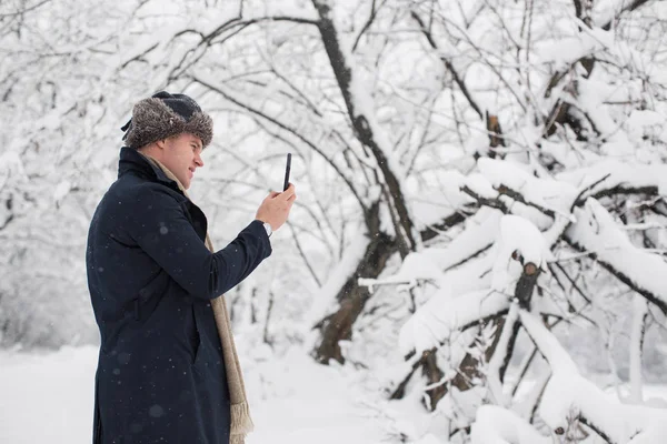 雪に覆われた公園に立って 携帯電話で写真を行う若い男の側面図 — ストック写真