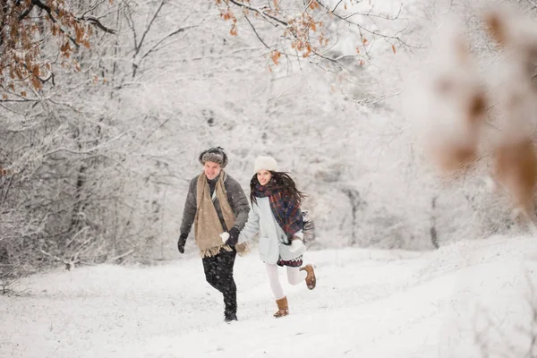 The young happy couple running in the snow-covered park outdoors