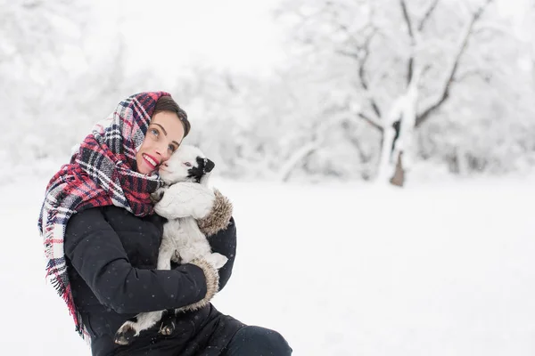 坐在雪地里抱着小山羊的微笑的年轻美丽的女人 拥抱在户外 — 图库照片