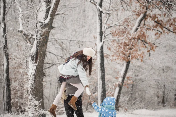 年轻人抱着快乐的妻子在怀里 小儿子在外面白雪覆盖的公园里把手递给她 — 图库照片