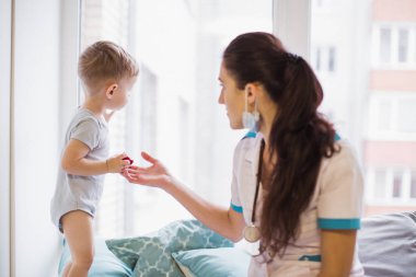 Koltuğun üzerinde duran ve pencereden bakarak komik küçük oğlan yakınındaki odasında bir kanepede oturan genç doktor