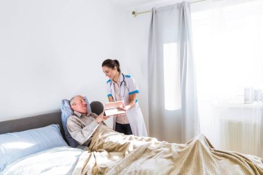 Bir yatak ve mutlu genç doktor onun yanında duran ve tablet onu odaya gösterilen yatan hasta, yaşlı, neşeli adam