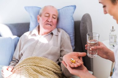 Yaşlı adam bir yatak ve bir doktor yanına oturmuş ve hapları vermeye yatan hasta ve ona su