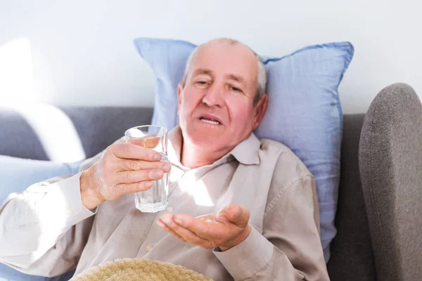 Portrait of the old sick man lying on a bed and drinking pills at home