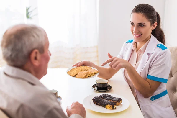 Die Junge Lächelnde Krankenschwester Sitzt Mit Dem Kranken Alten Mann — Stockfoto