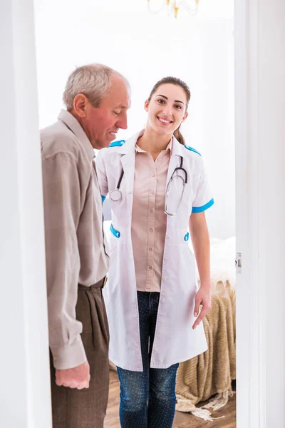 若い笑顔の看護師の近くに立っている老人の側面図 — ストック写真