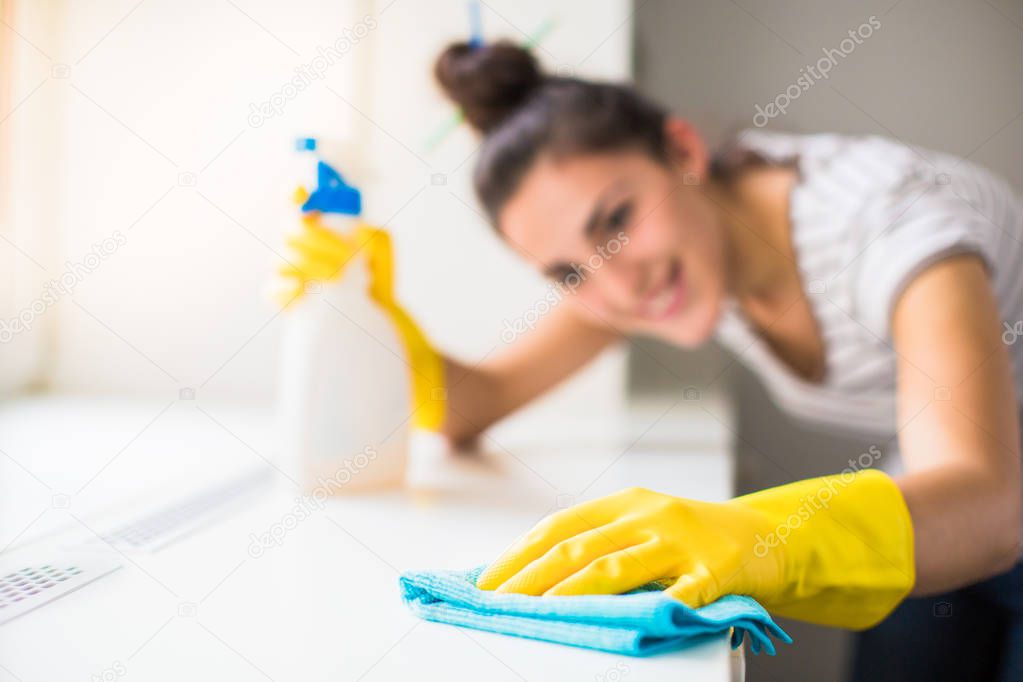 Close-up the young smiling woman in yellow gloves washing windowsill with rag and window cleaner indoors