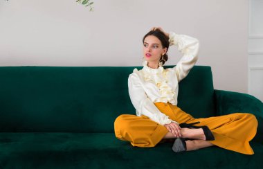 Bir yeşil kanepe kapalı ve görünümlü bir yana üzerinde oturan muhteşem, ciddi, şık genç kadın