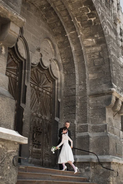古いビルドの階段を実行している花嫁を抱きしめる幸せな若い婚約者 — ストック写真
