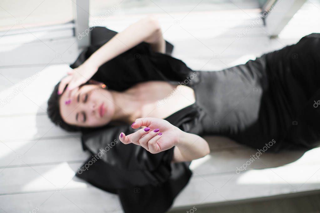 The young bewitching brunette woman in a black dress lying on the floor indoors