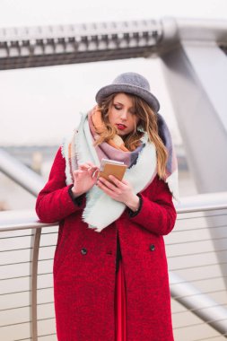 Açık ve telefon bakarak köprü üzerinde şapka duran genç güzel Bayan portresi