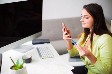 Kim ofiste oturan ve telefon ve kartvizit elinde tutan genç neşeli iş kadını görünümünü yan