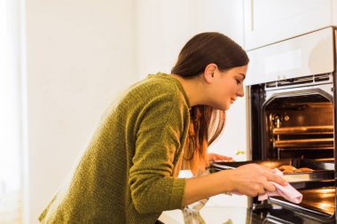 Genç neşeli kadın görünümünü pişmiş yemek arıyor ve mutfakta Fırından çanağı çekerek yan