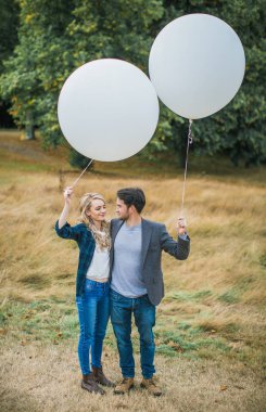 Yüz yüze açık duran ve beyaz balonlar elinde tutan genç romantik çift