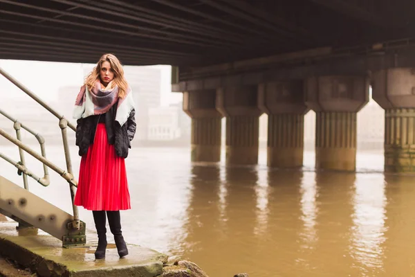The young beautiful serious lady standing outdoor by the river