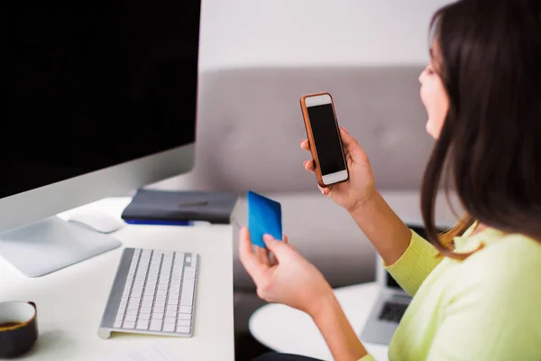 Side view of the young business woman who sitting in the office and holding the phone and business card in hands