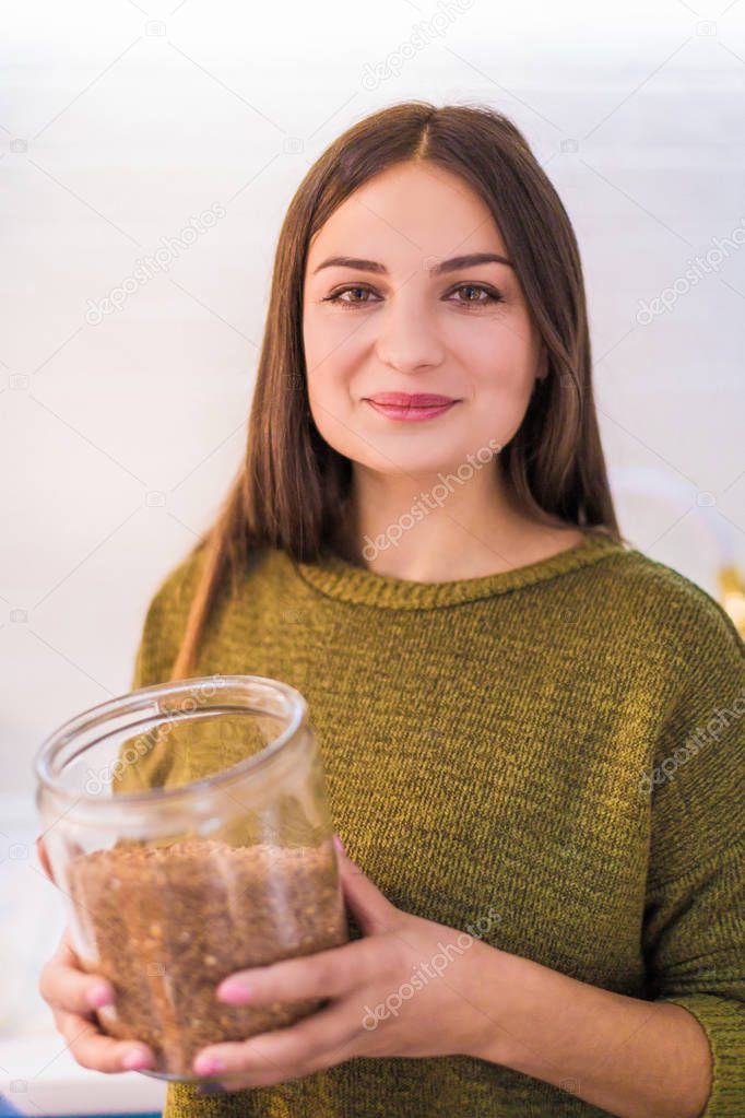 Portrait of the young happy woman who cooking in the kitchen and holding dish with buckwheat in hands