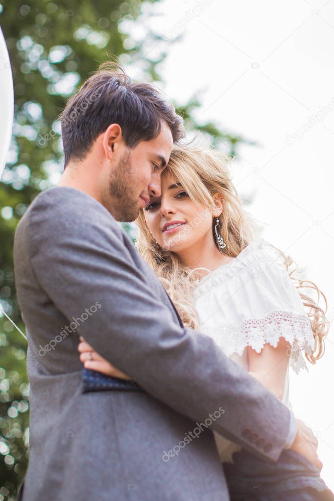 The young happy romantic couple standing in embrace on the sunlight outdoors