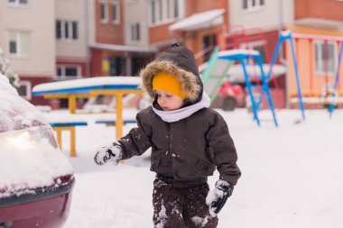 Bahçede duran ve kar ile oynayan sevimli küçük çocuk