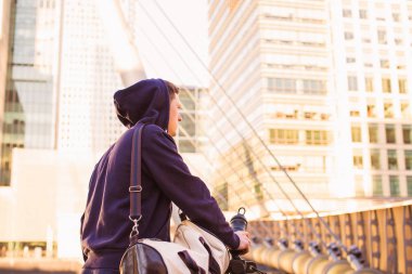 Arkadan görünüşü sportif delikanlı kim ayakta açık tutan sportif çanta ve şişe ve binalar üzerinde seyir