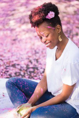 Yüzündeki boya ile açık oturma ve kuru boya elinde tutan genç gülümseyen kadın