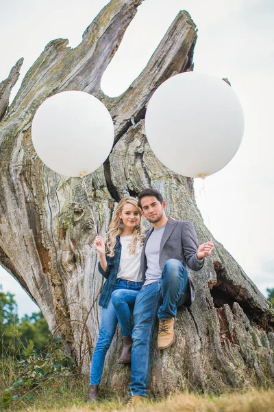 Kucaklama açık ve eski sandık ağacının güvenerek ayakta ve beyaz balonlar elinde tutan genç romantik çift