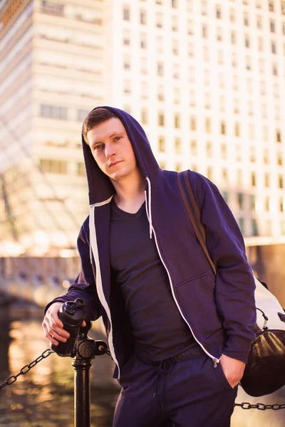 Portrait of young sporty man who standing outdoor by the river and holding sporty bag and bottle