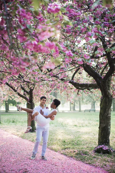 公園と腕の中で男持株女性に花びらで道路を歩く若い幸せなロマンチックなカップル — ストック写真