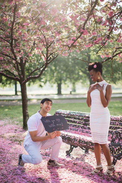 年轻人在公园里向年轻女子求婚 他拿着一张桌子 上面刻着 你会和我一起举起吗 — 图库照片