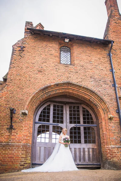 屋外の建物のドアの前に立っている若い陽気な魅力的な花嫁 — ストック写真