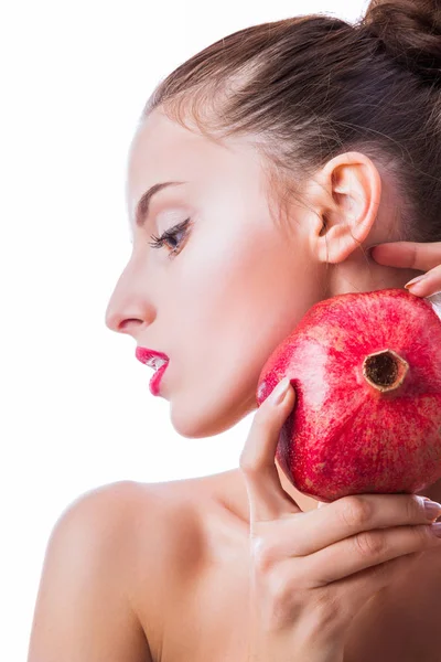 Side view of woman\'s face and pomegranate which she keeps near face in her hands indoor