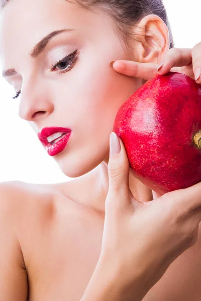 Close-up side of woman\'s face with makeup who keeps a pomegranate near face indoor