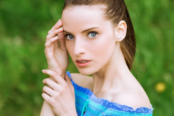 Portrait of young exquisite woman with bare shoulders who keeps hand on her face outdoor