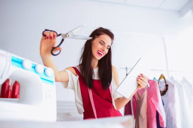Çekici gülümseyerek terzi oturur ve makas sağ el, sol elinde tablet tutar ve bu çalışma şeyler ile donatılmış oda bakar