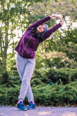 Genç sportif gülümseyen kadın parkta duruyor ve egzersiz