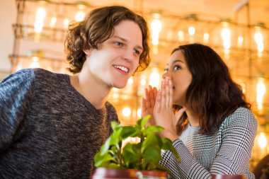 İki odaklı öğrenci kafede oturmak ve bir kadın için bir adamın kulağını, bir şey içeride konuşuyor