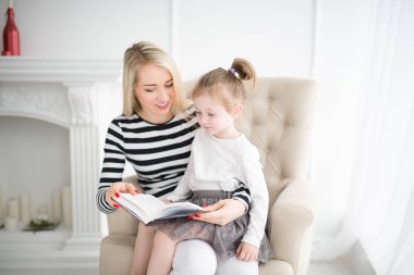 Güzel anne bir sandalyeye oturur ve kızı kucağına tutar, Anne kızı evde bir kitap okur