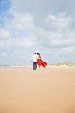 Arkadan görünüşü kucaklama kumsalda yürüyen genç bir romantik çift