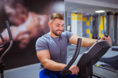 Yakın çekim gülümseyen yakışıklı eğitmen simülatör spor egzersizleri yapıyor