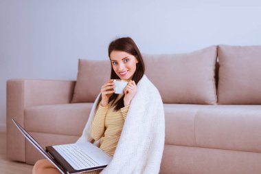 Gülümseyen güzel kadın kanepe laptop ile oturur ve çay içer