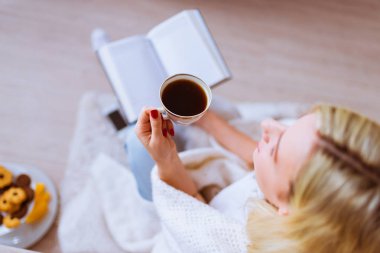 Güzel bir kadın oturur bir kitap ve evde, çay ile yere görüntülemek yukarıdan
