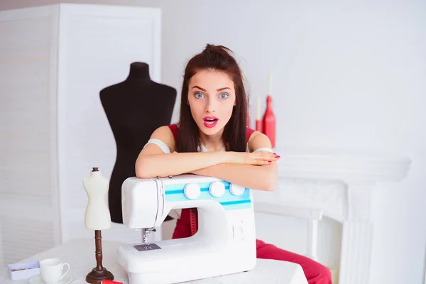 Exquisite happy seamstress sits at the table and relies on sewing machine in workshop