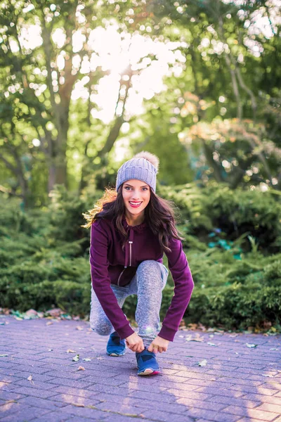 Young smiling woman squats in the park and adjusts her shoes