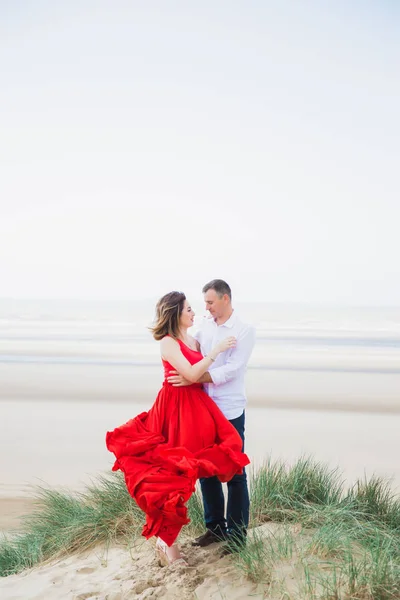 赤で幸せな女性は彼女の夫と抱擁で立っているし 海の背景に見て — ストック写真