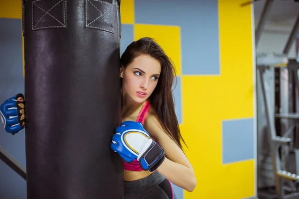 Close-up attractive fitness woman stands near punching bag dressed in boxing glove, at the gym