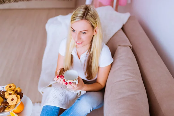 Mulher Sorridente Atraente Senta Sofá Com Copo Biscoito Suas Mãos — Fotografia de Stock