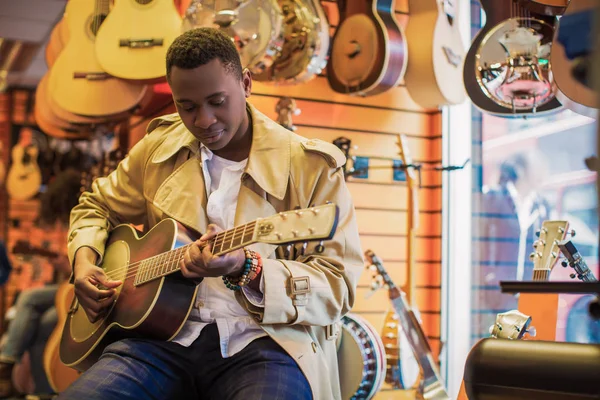 Handsome man sits and plays guitar in a guitar store