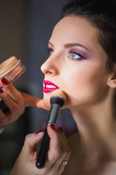 Makeup artist applies powder on a skin of face girll