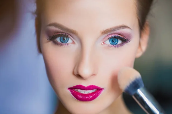 Makeup artist powders cheek of beautiful woman