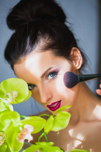 Beautiful face of woman with makeup on which makeup artist applies blush